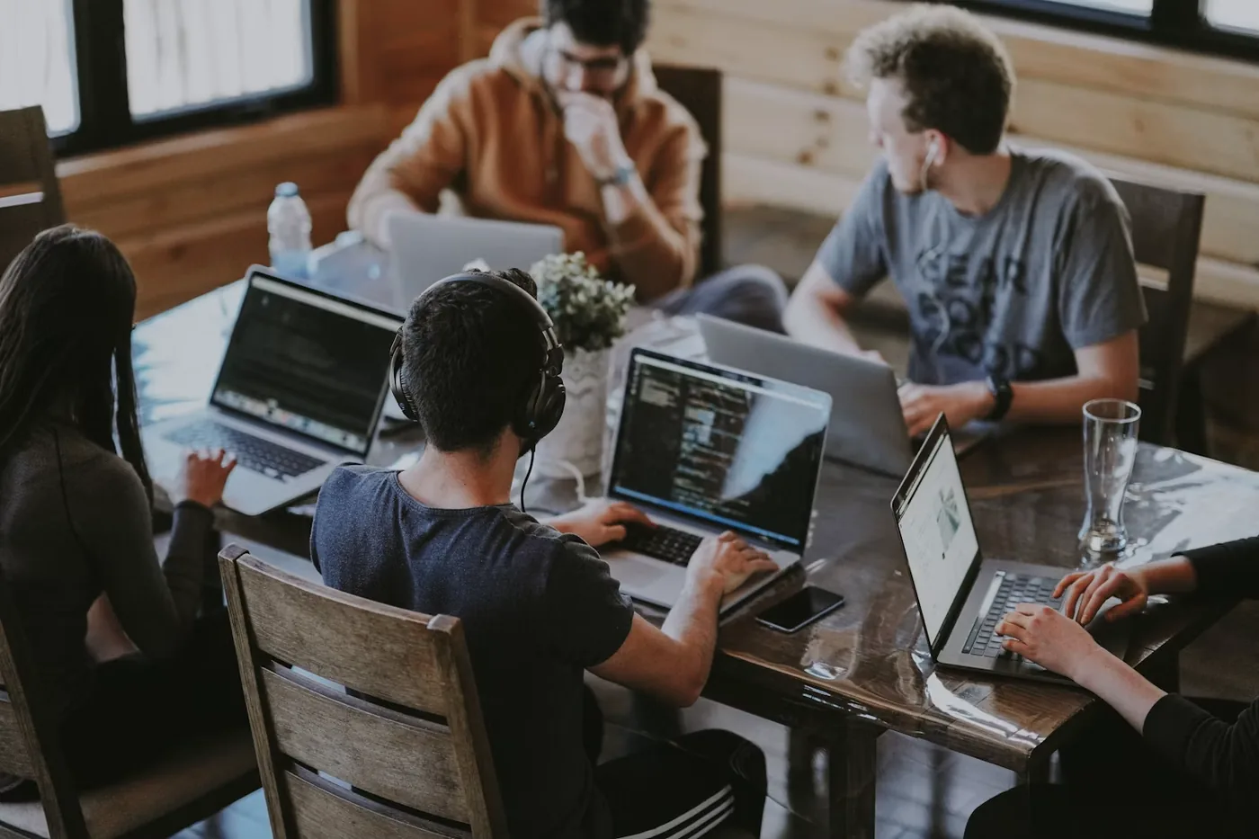 Cinco personas trabajando con portátiles alrededor de una mesa de madera